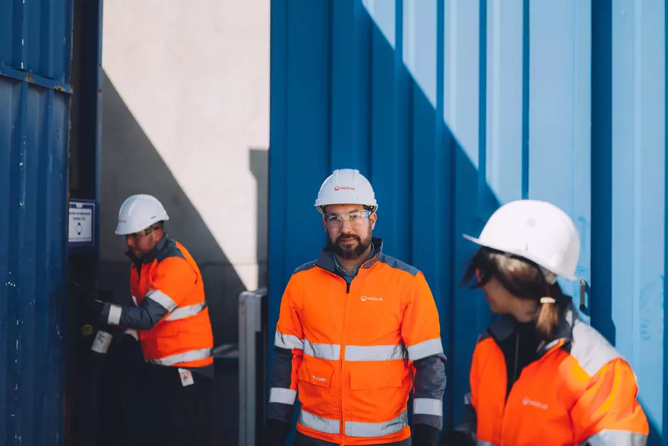Drei Veolia Mitarbeiter stehen vor einem blauen Container