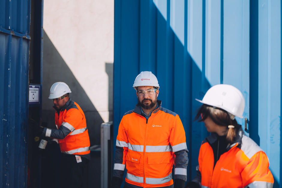 Drei Veolia Mitarbeiter stehen vor einem blauen Container