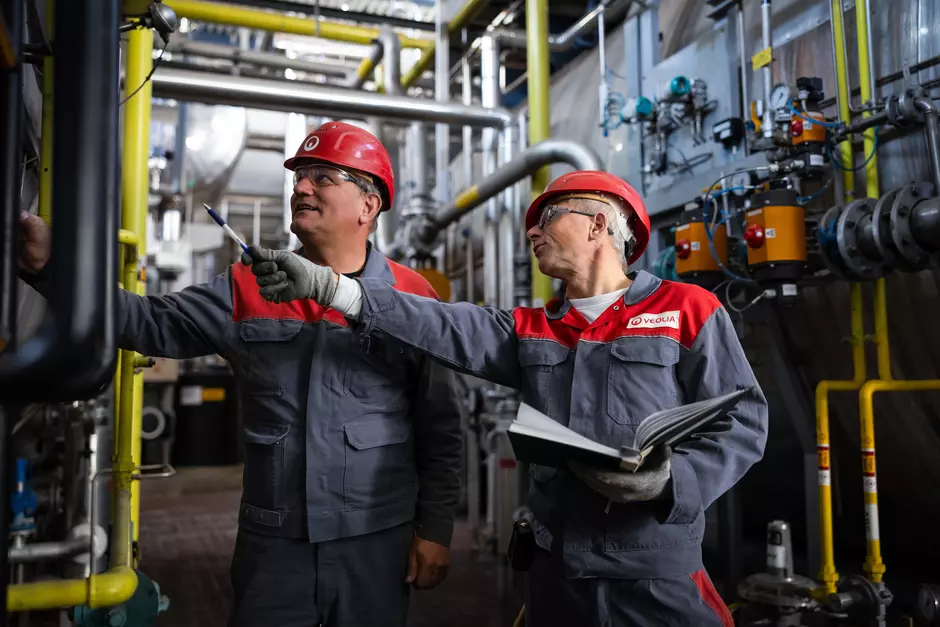 2 Veolia Mitarbeiter stehen in einer Produktionshalle und zeigen auf etwas dort