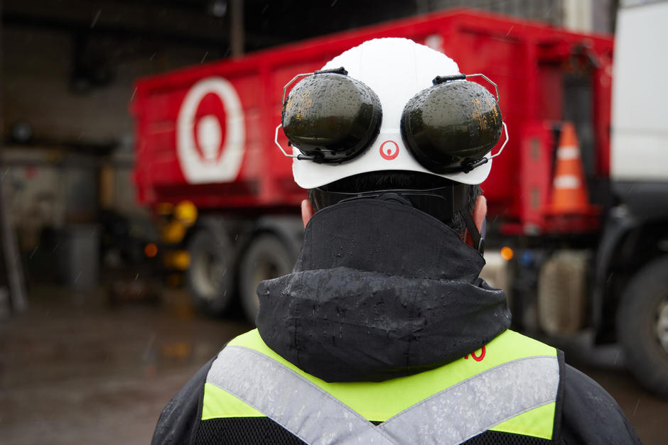 Veolia Mitarbeiter von hinten mit Sicherheitshelm und Lärmschutz, im Huntergrund ein Veolia Auto